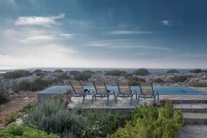 Zona de piscina con sillas de descanso y vista al océano.