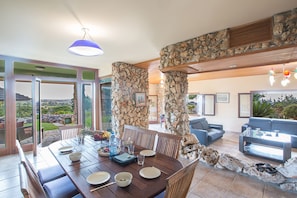 A dining area with a stone pillar, a blue hanging light, and a view of the outdoors.