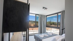Ett modernt hotellrum med en stor säng, utsikt över landsbygden och en balkong.