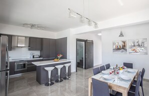 Een moderne keuken met een centraal eiland, krukken en een eethoek met een tafel voor zes personen.