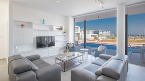 Un salon moderne doté d’un grand téléviseur, de canapés gris, d’une table basse et offrant une vue sur une piscine et des immeubles.