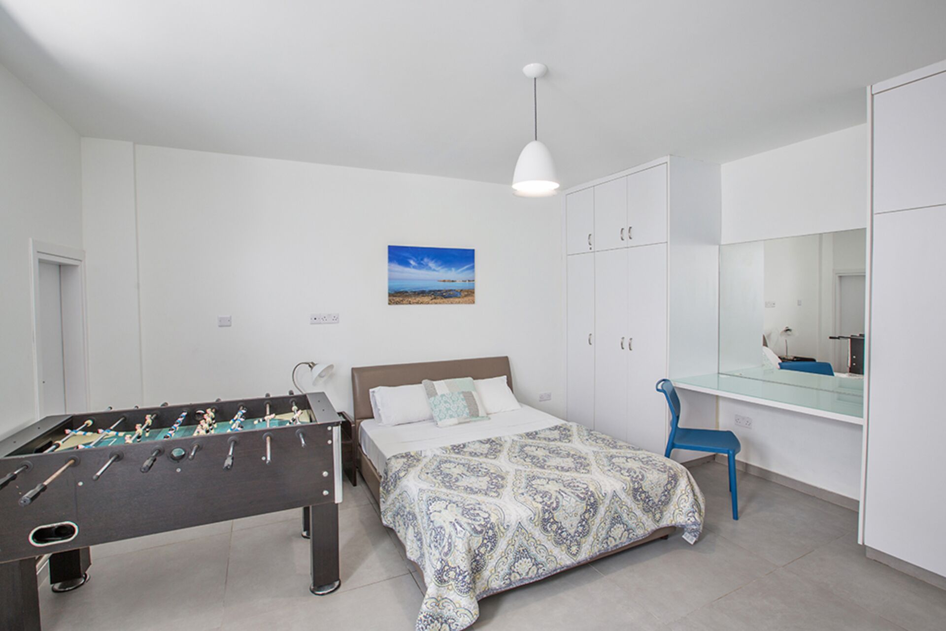 A bedroom with a bed, a foosball table, a desk with a chair, a mirror, and a wardrobe.