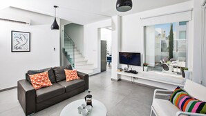 Un salon moderne avec un canapé, une table basse et un téléviseur. Un escalier mène à un autre niveau.