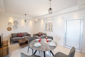 Ein modernes Wohnzimmer mit einem runden Esstisch für vier Personen, zwei Sofas, einem Fernseher und dekorativen Tellern an der Wand.