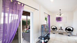 A modern living room with a TV, two black chairs, a table with a vase of flowers, and a purple curtain. - The Complete Guide to Renting Your Exclusive Holiday Villa in Protaras with Private Pool and Close to the Beach (Protaras)