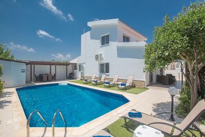 A modern poolside area with a clear blue pool, sun loungers, and a white building with multiple windows. - The Complete Guide to Renting Your Exclusive Holiday Villa in Protaras with Private Pool and Close to the Beach (Protaras)