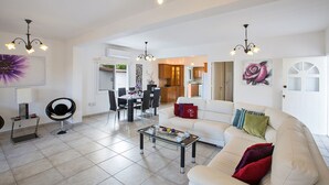 A spacious living area with a sofa, coffee table, and dining table. There is a kitchen area visible through an open doorway. - The Complete Guide to Renting Your Exclusive Holiday Villa in Protaras with Private Pool and Close to the Beach (Protaras)