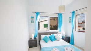 A bedroom with a bed, two bedside tables, a window with curtains, and a view of buildings outside. - The Complete Guide to Renting Your Exclusive Holiday Villa in Protaras with Private Pool and Close to the Beach (Protaras)