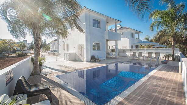 Ett modernt hus med en swimmingpool, utomhusmöbler och palmer.