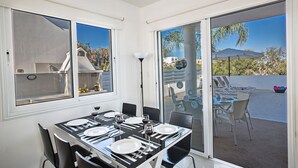 En matplats med ett bord för fyra personer, en grill och utsikt över en pool och palmer.