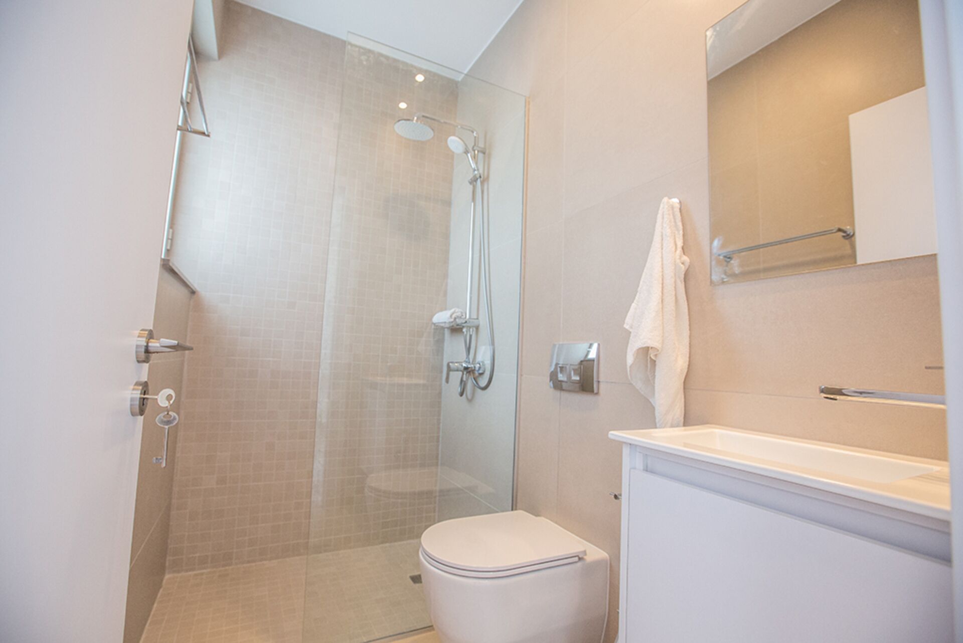 A modern bathroom with a glass-enclosed shower, a white toilet, and a vanity with a mirror and towel rack.