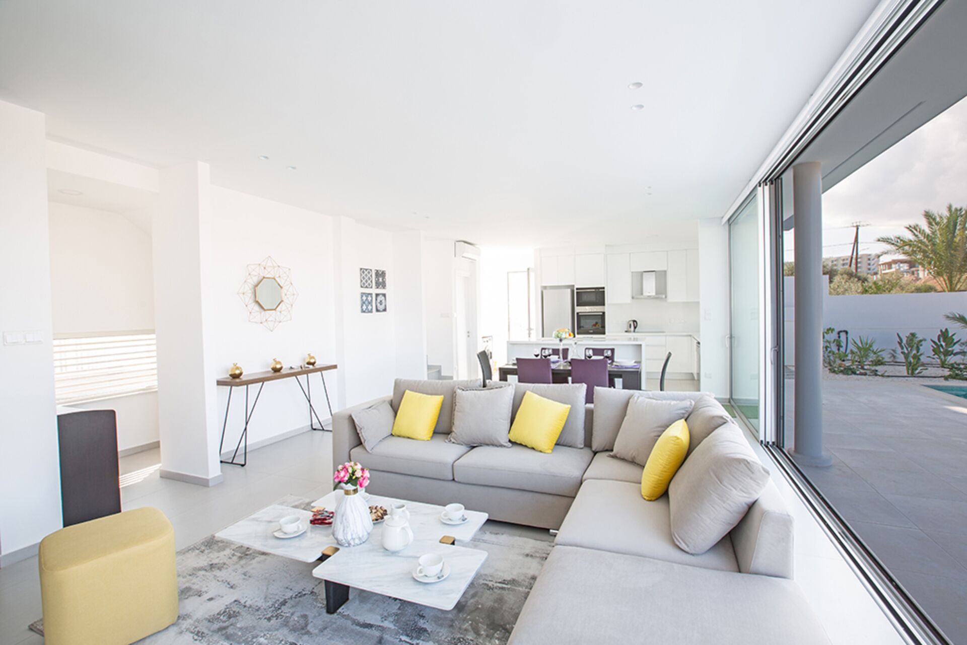 A modern living room with a grey sofa, yellow cushions, a coffee table, and a dining area in the background.