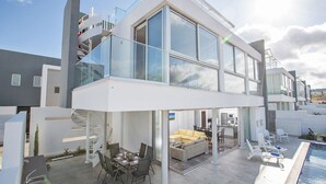 A modern two-story house with a glass balcony, outdoor seating area, and a swimming pool. - Your Dream Holiday Villa with Private Pool in Protaras most Exclusive Neighbourhood (Protaras)