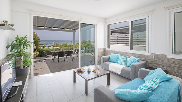 A modern living room with a sofa, coffee table, and a view of the sea through large glass doors.