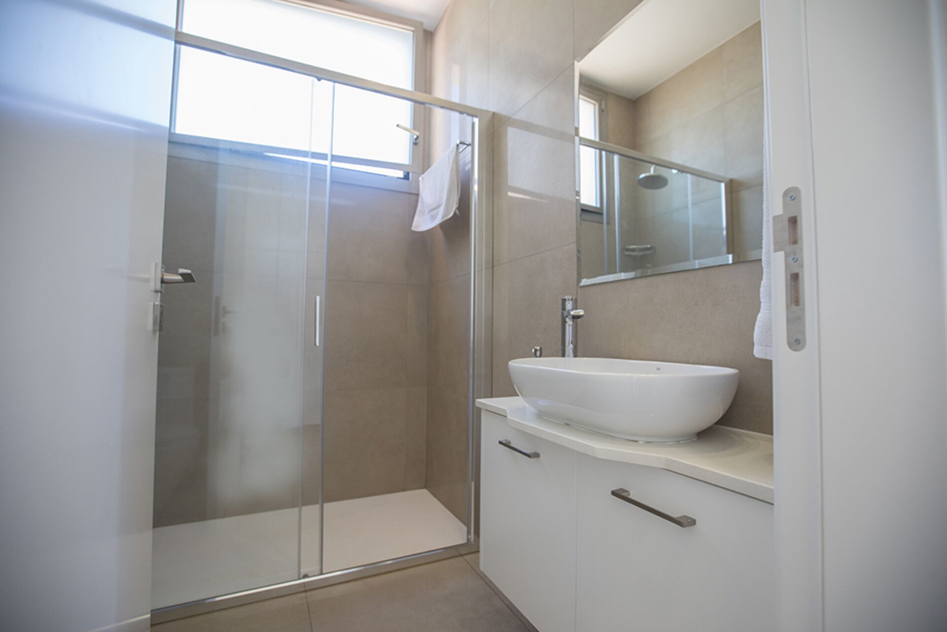 Un baño moderno con cabina de ducha de vidrio, un lavabo blanco y un espejo encima.