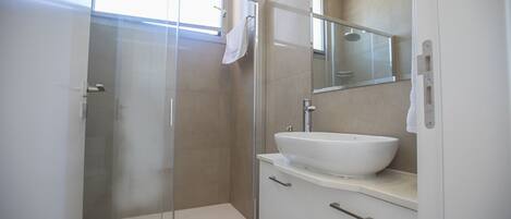 Un baño moderno con cabina de ducha de vidrio, un lavabo blanco y un espejo encima.