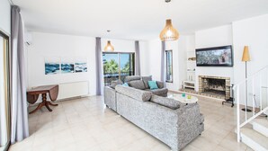 Un moderno salón con un sofá gris, una chimenea, un televisor y un balcón con vistas.