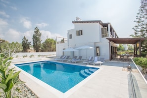 Une maison moderne à deux étages, dotée d’une piscine, de chaises longues et d’un patio couvert.
