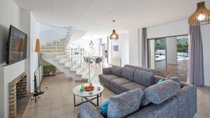 Un espacio habitable amplio con un sofá gris, una mesa de centro y una escalera que sube a un piso superior.