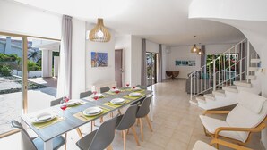 Un comedor moderno con una larga mesa preparada para cuatro personas, una escalera y vistas al exterior.