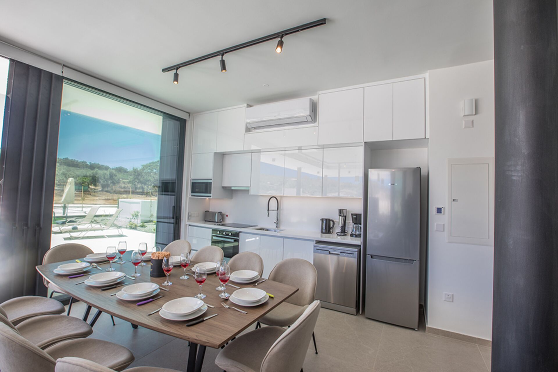 Cocina moderna con armarios blancos, electrodomésticos de acero inoxidable y comedor con mesa dispuesta para seis personas.