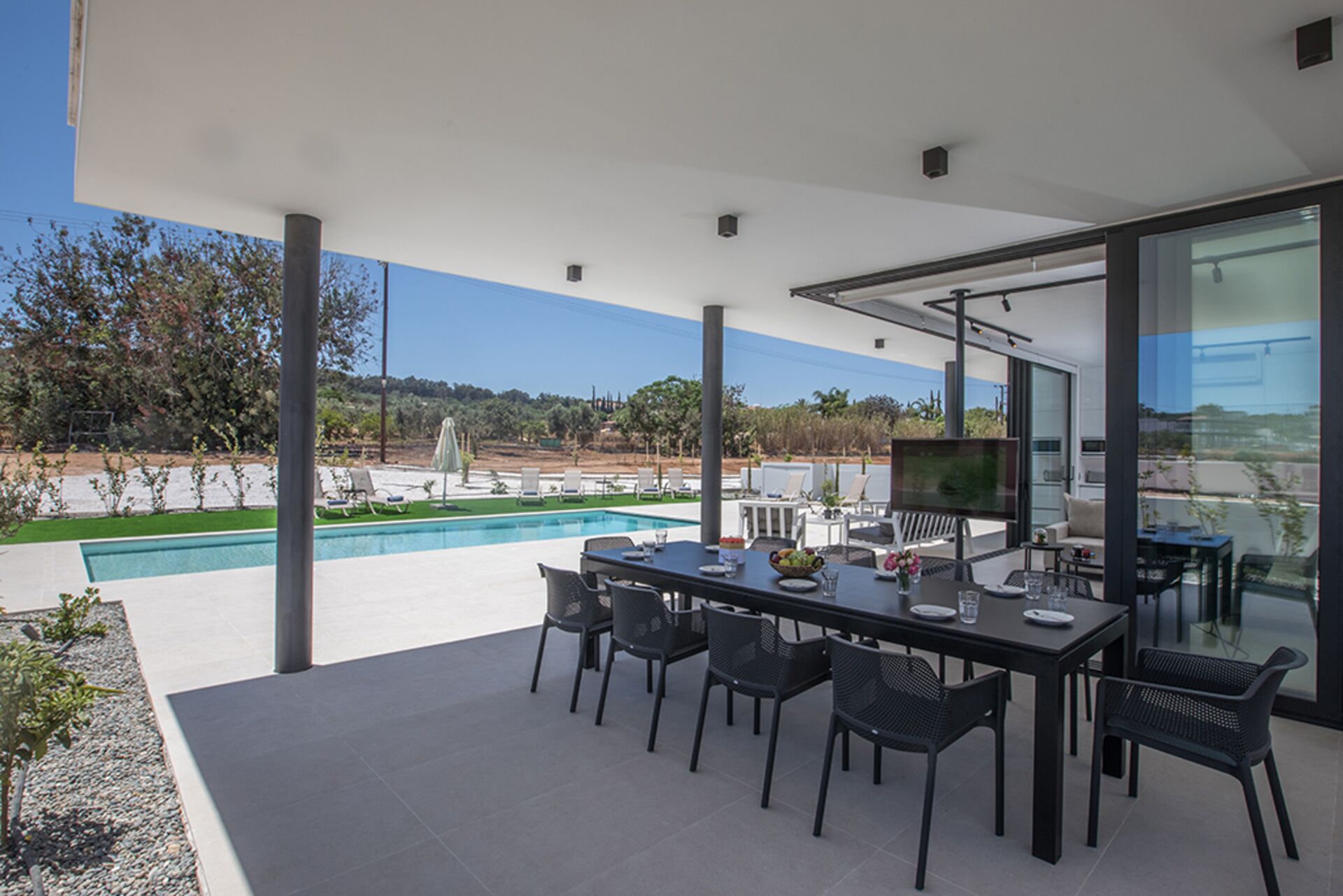Un espace de restauration extérieur moderne, doté d’une piscine, qui offre une vue sur un jardin aménagé et un ciel dégagé.