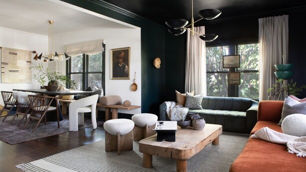 Una sala de estar moderna con una pared de acento verde oscuro, una mesa de centro de madera y un sofá con una manta.