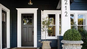 Una casa azul oscuro con puerta principal blanca, el número 212 a la derecha y una planta en maceta en el porche.