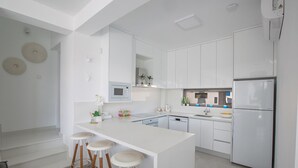 A modern kitchen with white cabinetry, a central island with stools, a built-in oven, and a stainless steel refrigerator. - The Complete Guide to Renting Your Exclusive Holiday Villa in Protaras with Private Pool and Close to the Beach (Protaras)