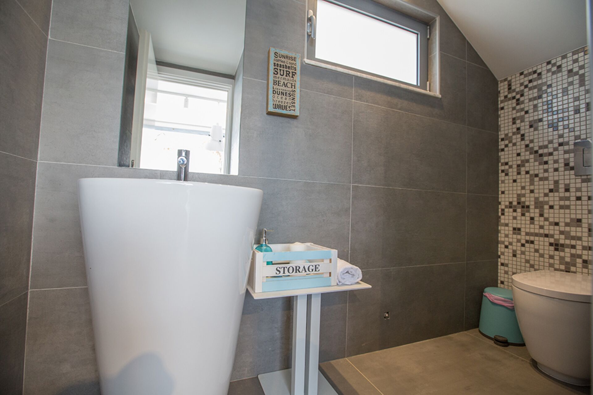 A bathroom with a large white sink, a small window, and a tiled wall.