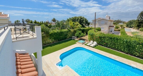 A swimming pool with a small deck area, surrounded by a well-maintained lawn and hedges.
