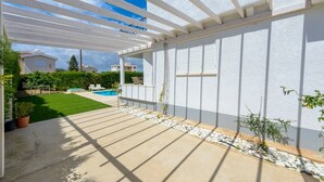 Ein überdachter Patio-Bereich mit Pool, Kübelpflanzen und Blick auf benachbarte Häuser.