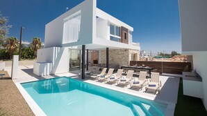 Ett modernt hus i två våningar med en swimmingpool, en uteplats och utsikt över staden.