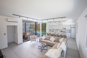 Una sala de estar moderna con un sofá, una mesa de centro y sillas. Se ve una piscina a través de las puertas de cristal.