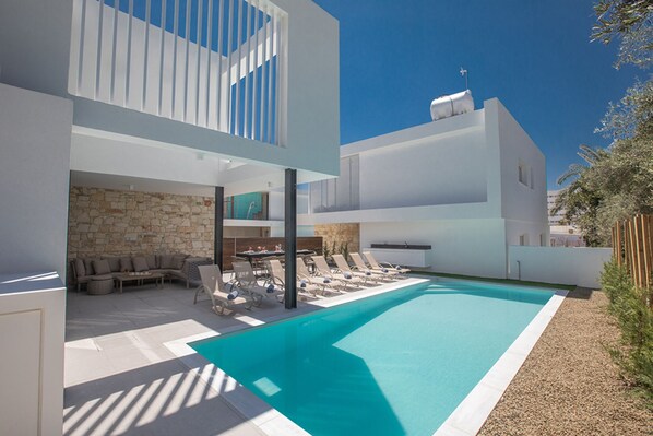 Un área de piscina moderna al aire libre con pared de piedra y sillones de descanso.