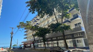 A multi-story building with balconies, a parking area, and a clear blue sky. - Loft Vista Mar (Guarapari)