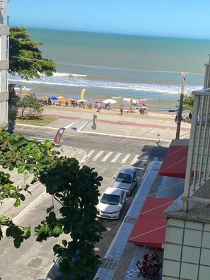 A street view with a beach in the background, cars parked along the road, and a pedestrian crossing. - Loft Vista Mar (Guarapari)