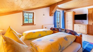 Un plafond en bois, deux lits avec une literie à motifs floraux, une télévision et une armoire.