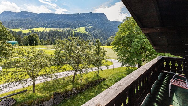 Un balcon donnant sur une vallée verdoyante et des montagnes.