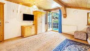 A wooden interior with a television, cabinets, a patterned rug, and a view through a glass door. - Apartment 'Jägermeister' with Mountain View, Shared Garden and Wi-Fi (Sankt Martin bei Lofer)