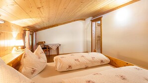 A room with wooden ceiling beams, a bed with floral bedding, a small table with a lamp, and a chair. - Apartment 'Jägermeister' with Mountain View, Shared Garden and Wi-Fi (Sankt Martin bei Lofer)