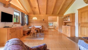 Une pièce spacieuse avec des poutres en bois, un coin repas, un téléviseur et des meubles de rangement en bois.