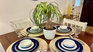 Ein Esstisch ist mit blau-weißen Tellern, Besteck und klarem Glas gedeckt, wobei eine Topfpflanze im Mittelpunkt steht.