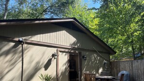 Ein überdachter Patio-Bereich mit Tisch und Stühlen, einer Kübelpflanze und einem Holzzaun im Hintergrund.