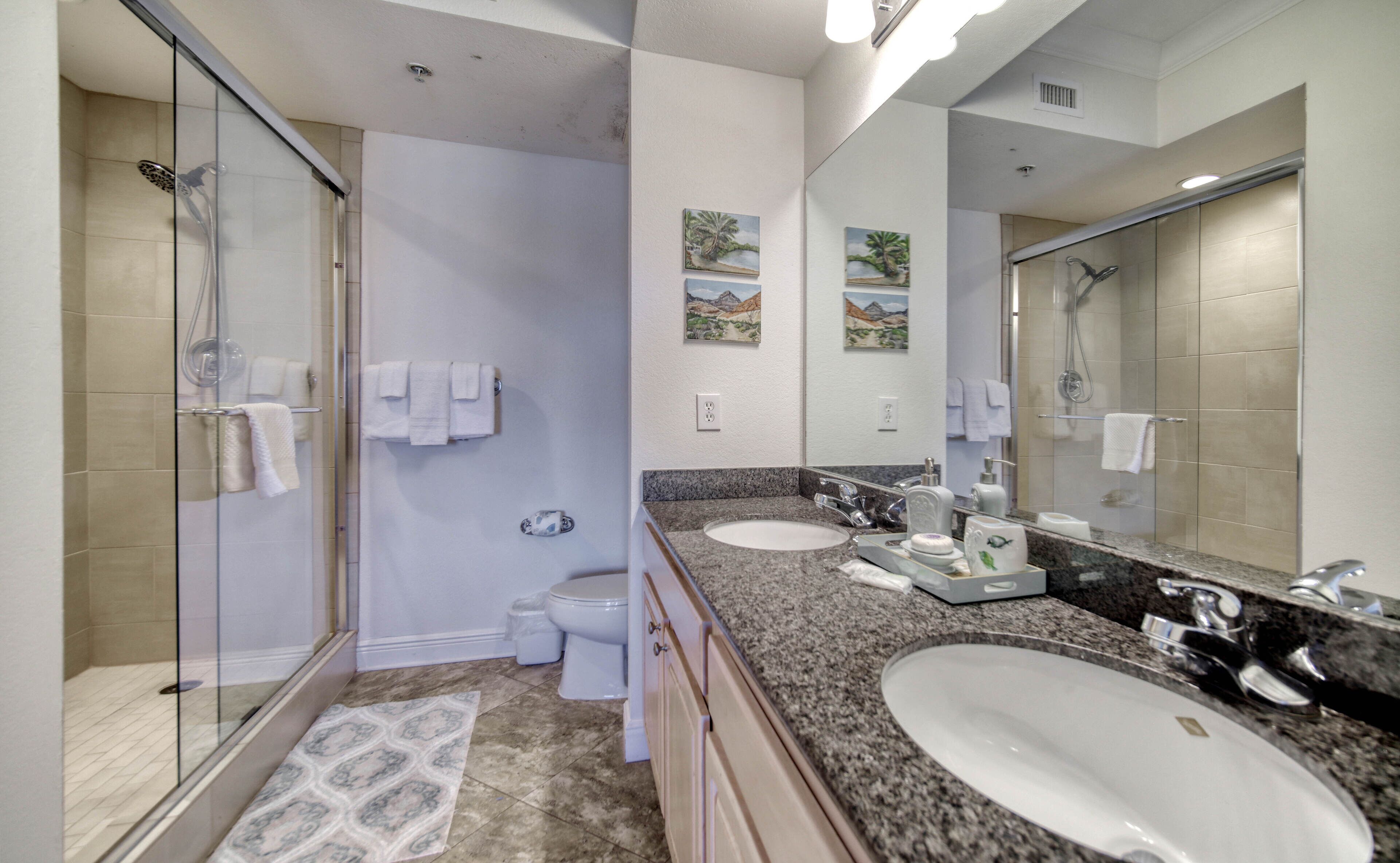 A modern bathroom with a glass shower enclosure, two sinks, a large mirror, and decorative wall art.