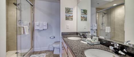 A modern bathroom with a glass shower enclosure, two sinks, a large mirror, and decorative wall art.