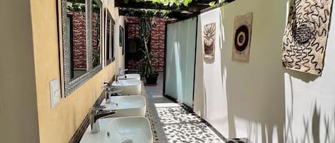 A narrow corridor with a row of sinks and mirrors on one side, a tiled floor, and artwork on the walls.