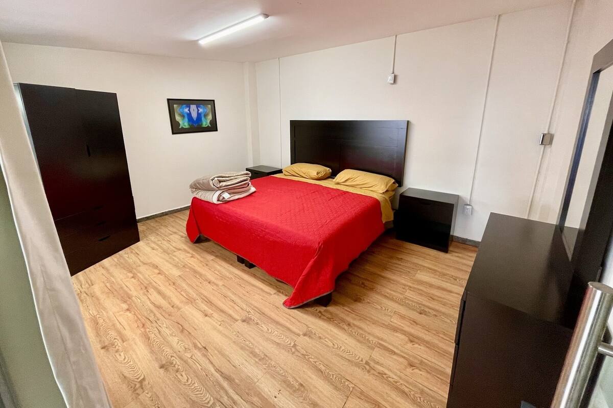 Une chambre d’hôtel avec un lit, une table de chevet, un plancher en bois, un tableau au mur et une porte.