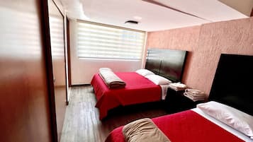 A hotel room with two beds, a large window with blinds, a wooden floor, and a dark headboard.