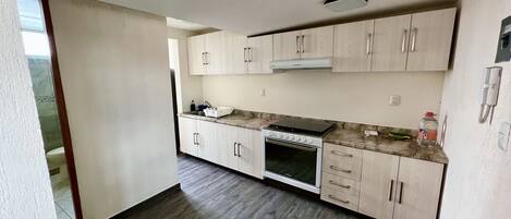 Una cocina moderna con armarios de madera clara, horno de acero inoxidable y encimera de mármol.